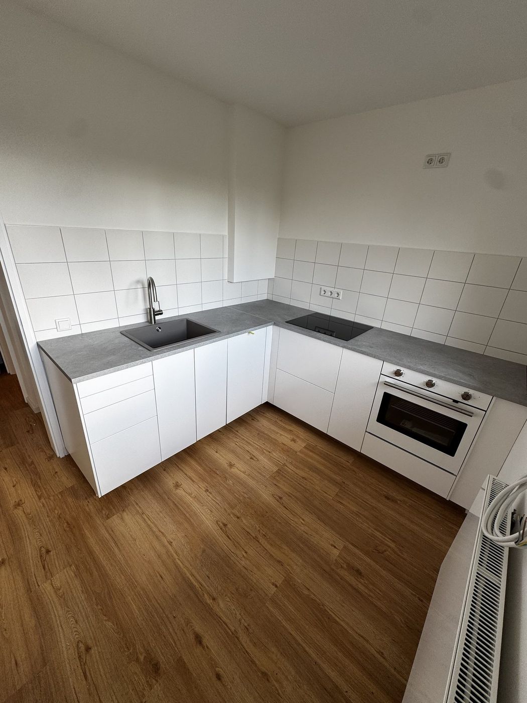 Fertig montierte weiße Einbauküche mit grauer Arbeitsplatte auf Holzboden